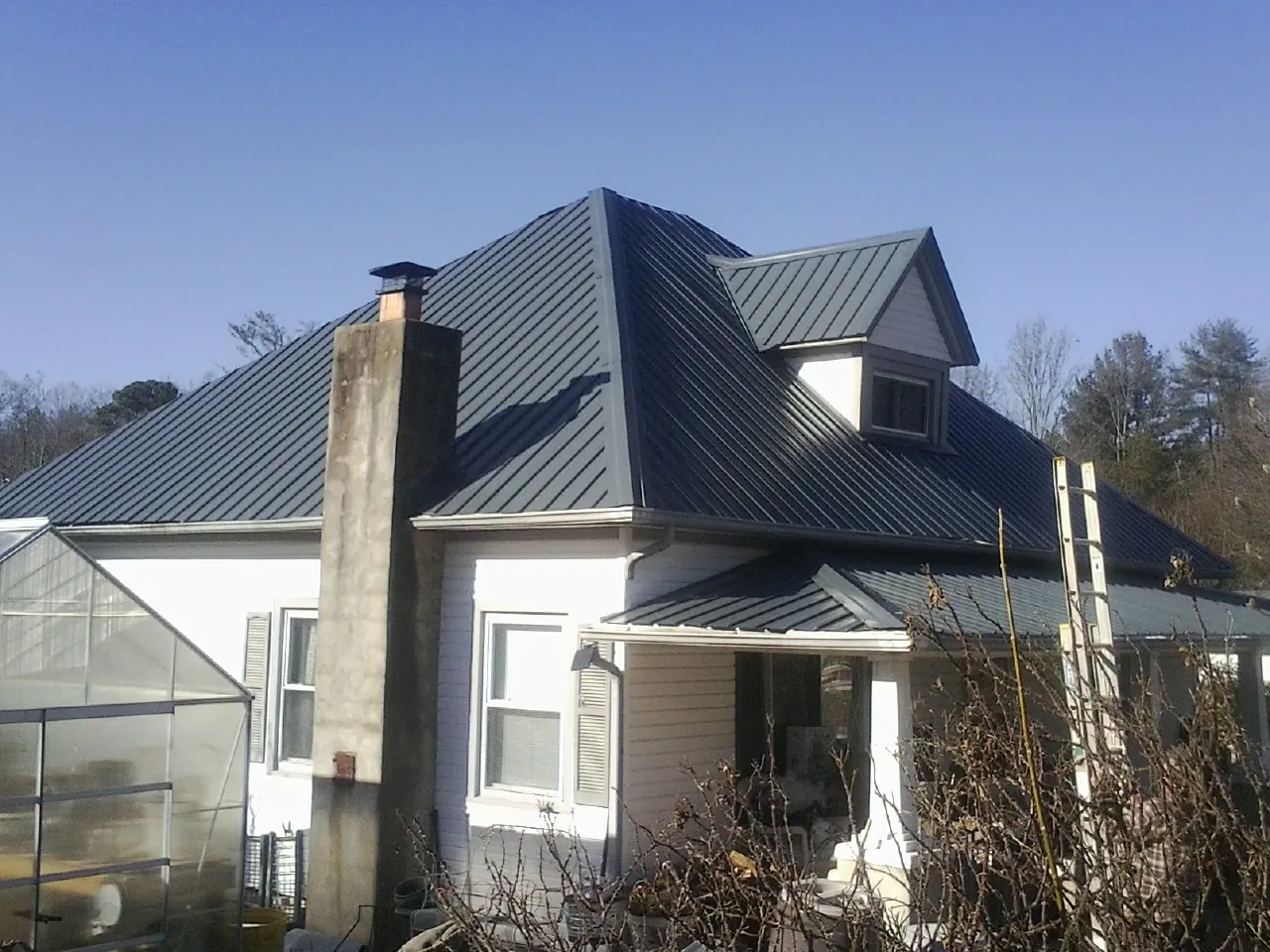 Dark blue standing seam metal roof on a white farmhouse with dormer — Slate & Tile Roof Repair by Roofing Brothers in Icard