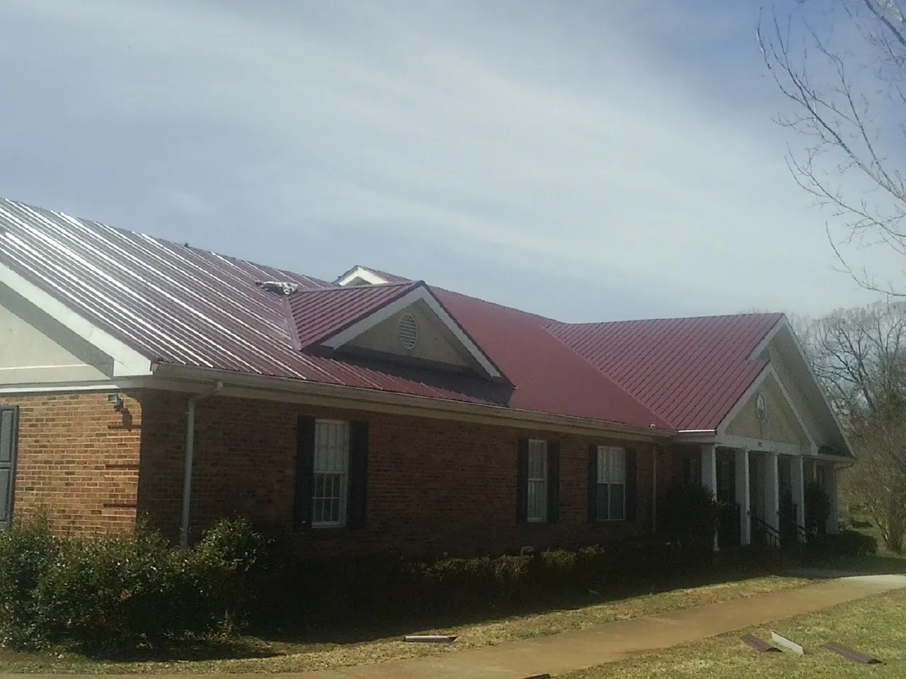 Red metal roof with gabled entries on a long brick building, from a Hail Damage Roof Repair job in Icard