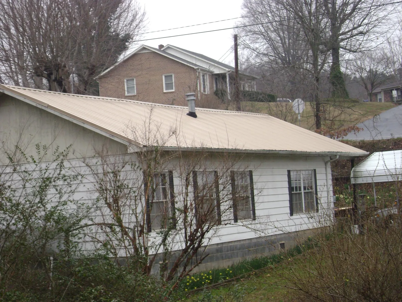 Tan metal roof on a white sided house set into a hillside — Commercial Roofing by Roofing Brothers in Icard